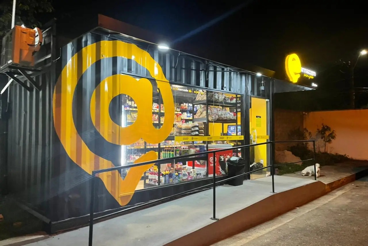 Loja Armazzem em container, iluminada à noite, com o símbolo @ gigante pintado em amarelo